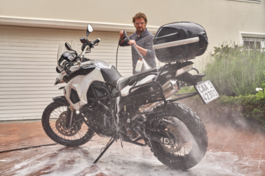 Mann wäscht eine weiße Reiseenduro-Motorrad mit Hochdruckreiniger.